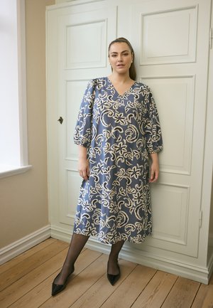 Modrá květinová šatová vzorovaná šaty s véčkovým výstřihem, tříčtvrtečními rukávy a splývavým designem. Nosit s černými podpatky a průhlednými punčochami.