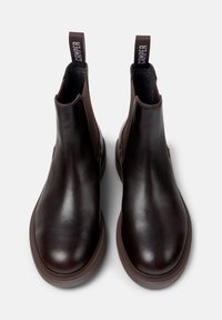 Les bottes Chelsea en cuir marron présentent des panneaux latéraux élastiques, un bout arrondi et une semelle en caoutchouc texturé. Onglet avec le logo "Camper" à l'arrière.