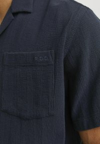 Marineblauwe korte mouwen shirt van textuurstof, met een borstzak met "R.D.D." borduring. Effen kleur, eenvoudig kraagontwerp.