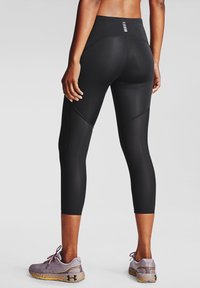 Svarta sportleggings med hög midja, med en texturerad paneldesign och en slät yta. Bärs med lila sportskor.