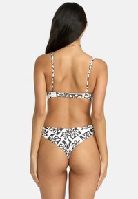Bikini floreale in bianco e nero con sottili spalline, chiusura posteriore regolabile e parte inferiore a taglio alto che mette in evidenza un motivo di grandi dimensioni.