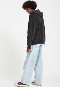 Sudadera negra con textura suave, con capucha ajustable, combinada con jeans anchos de color azul claro y zapatillas moradas.