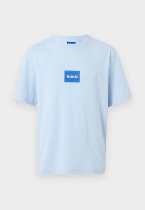Ανοιχτό μπλε κοντομάνικο T-shirt με ένα μπλε τετράγωνο λογότυπο τοποθετημένο στο κέντρο του στήθους που απεικονίζει τη λέξη "HUGO" με λευκά γράμματα.