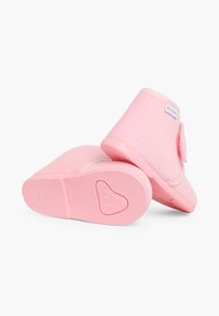 Des chaussons roses à enfiler, avec une texture à côtes, une forme arrondie et une semelle en caoutchouc à motif en cœur. Comprend un accent en tissu sur le côté.
