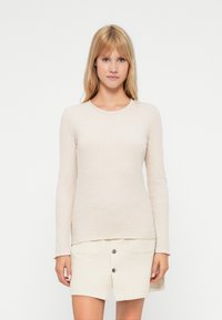 Beige langermet topp med ribbestruktur og rund hals, kombinert med et lyse farget skjørt med frontknapper og lommer.