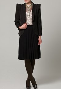 Svart skräddarsydd kavaj med axelvaddar, krämfärgad blus med prickar, svart plisserad kjol, mörkbruna strumpbyxor och svarta högklackade skor.