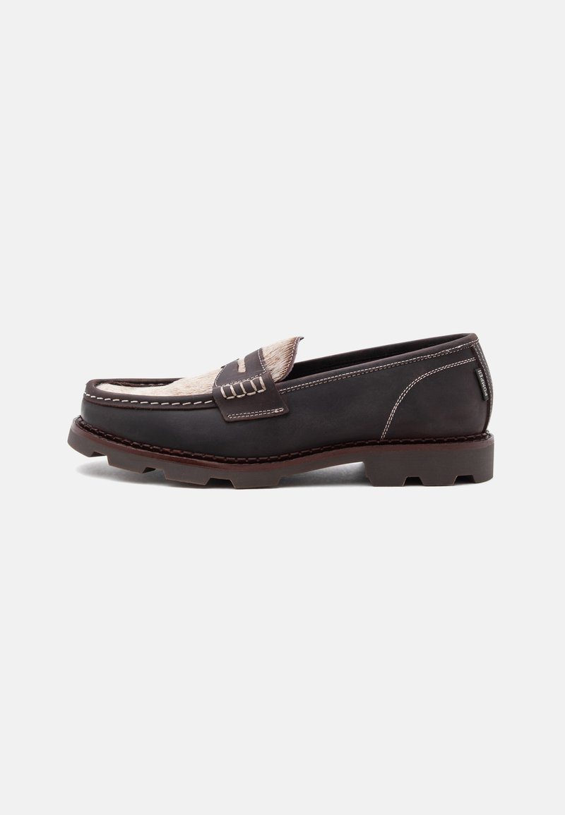 Mocassin en cuir brun foncé avec un détail en fourrure claire sur le dessus, coutures blanches, semelle épaisse à relief et petit talon, vu de profil.