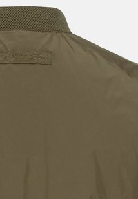 Olijfgroene windbreaker met een textuur en gebreide kraag, voorzien van een gladde, lichte stof en een gestikt merklabel op de achterkant.