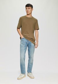 Oliwkowa koszulka z krótkim rękawem i okrągłym dekoltem, zestawiona z jasnoniebieskimi prostymi dżinsami i beżowymi trampkami z szarymi akcentami.