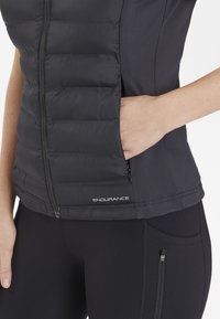 Svart pufferväst med horisontella sömmar, med en framsida som har blixtlås och en sidoficka. Materialet är slätt med en matt finish.
