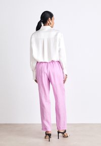 Chemise blanche à manches longues avec une coupe décontractée, associée à un pantalon rose clair ample et des sandales à talons hauts noires. Design et textures simples.