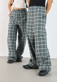 Weite Karottenhosen aus Karomuster in Schwarz, Grün und Weiß, mit einem bequemen Bund, Seitentaschen und einem logierten Detail an einem Bein.