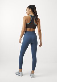 Barna sportmelltartó kék részletekkel, magas derekú kék leggings és világoskék sportcipők. Simább anyag, testhezálló fazon, minimális stílus.
