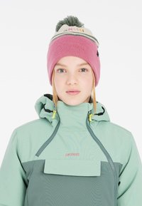 Gorro con base rosa, banda blanca y pompón verde. Chaqueta en tonos de verde menta con bolsillo y cremallera en verde oscuro que contrastan.