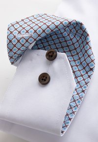 Valge särgi mansett, millel on pruunid nööbid ja sees mustriline krae, kus on sinised õied pruunide kuusnurkade sees.