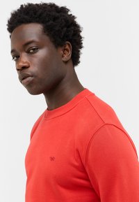 Czerwona bluza z bawełny z okrągłym dekoltem, ściągaczami i małym haftowanym logo na piersi. Miła w dotyku, luźny krój.