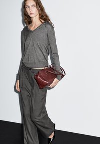 Grijze textuur met lange mouwen gecombineerd met brede gestreepte broek. Een kleine bordeaux leren handtas voegt contrast toe. Glad zwart schoeisel maakt de look compleet.