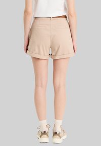 Beige Baumwollshorts mit umgeschlagenen Säumen, zwei Gesäßtaschen und einem geflochtenen Gürtel, kombiniert mit Sneakers und weißen Socken.