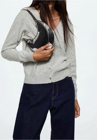 Szary kardigan z guzikami, noszony z ciemnymi dżinsami; trzyma czarną, zakrzywioną torebkę z błyszczącym wykończeniem i paskiem.