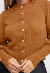 Hnědý pletený cardigan s kulatým výstřihem, který má pět knoflíků ve tvaru drahokamů vpředu a ribovanými manžetami pro texturovaný look.