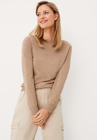 Maglione beige a maglia con colletto e polsini a coste, abbinato a pantaloni cargo beige chiaro. La texture sembra morbida e informale.
