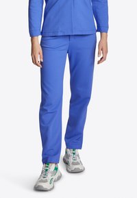 Person in blauen, geraden Hosen und weißen Sneakers mit grünen Akzenten, der vor einem schlichten weißen Hintergrund steht.