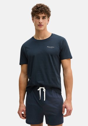 Young man wearing navy blue Marc O’Polo t-shirt and matching shorts with white drawstring, standing against plain light background.