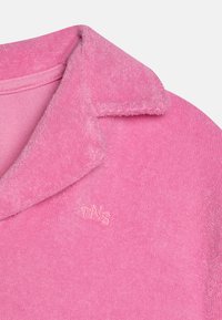 Rosa fleece-polo skjorte med krage, med en teksturert overflate og brodert "TNS"-logo på venstre side.