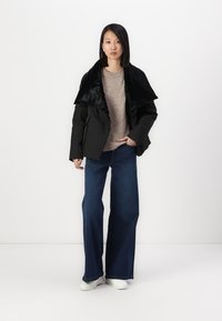 Black puffer jacket with a shiny oversized collar, paired with a light beige sweater and wide-leg blue jeans. White sneakers complete the look.