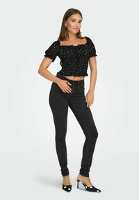 Czarna bluzka w groszki, krótka, z bufiastymi rękawami i marszczeniem, w połączeniu z wysokim stanem czarnych skinny jeansów oraz klapkami w groszki.