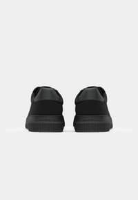 Zwarte sneakers met een gladde stof bovenkant en rubberen zool, met een getextureerde achteraccent en branding op de hiel. Minimalistisch ontwerp.