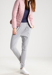 Vaaleanpunainen tikattu takki, jossa on istuva malli, yhdistettynä harmaisiin kapeneviin collegehousuihin. Valkoiset lenkkikengät viimeistelevät rentoa ilmettä.