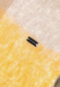 Tkanina z mieszanki wełny w kolorach żółtym, beżowym i szarym o miękkiej, puszystej fakturze. Zawiera małą metaliczną metkę z logo marki.