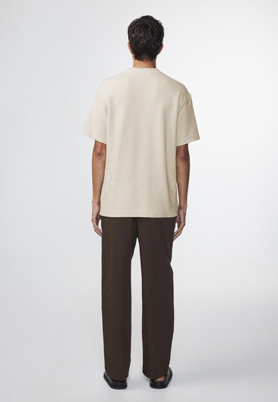 Beige tekstureret short-sleeve skjorte med lige snit, parret med mørkebrune brede bukser. Simpelt design, minimale accenter og neutrale farver.
