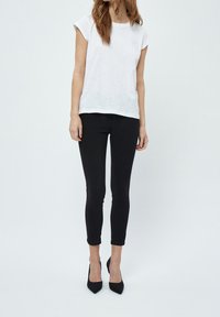 T-shirt blanc à manches courtes associé à des leggings noirs ajustés et des escarpins noirs à talons pointus. Tissu lisse avec une coupe décontractée.