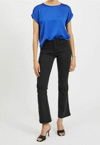 Kungsblå satinblus med rullade ärmar, matchad med högmidjade svarta utsvängda jeans och svarta öppna klacksandaler.