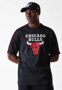 Melna acs džersija ar sarkanām akcentiem un tekstu "CHICAGO BULLS". Priekšā atrodas bullis grafika. Nēsā kopā ar atbilstošu melnu cepuri.