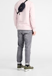 Grå avsmalnande byxor, ljusrosa sweatshirt, gröna sneakers och marinblå midjeväska. Strukturerat tyg med en avslappnad passform. Justerbar rem på väskan.