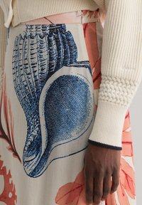 Gonna a fiori in morbido tessuto, con un'illustrazione dettagliata di una conchiglia blu. Maglione beige a coste con dettagli testurizzati sulle maniche.