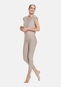 Set di activewear beige chiaro composto da una maglietta a maniche corte e leggings fino ai polpacci, realizzati in tessuto liscio e elastico. Tiene in mano una bevanda.