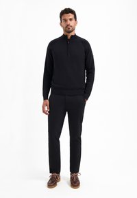 Zwarte rits-hals pullover met ribgebreide manchetten en onderrand, gecombineerd met zwarte broek en bruine leren schoenen met een gestructureerde zool.