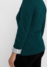 Teal langemouw shirt met een fitted design, voorzien van witte streeppatroon manchetten en een zachte, gladde stofstructuur.
