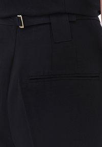 Zwarte stoffen broek met een gladde textuur, riemlussen, een slank ontwerp en een verborgen achterzak met een fijne afwerking.
