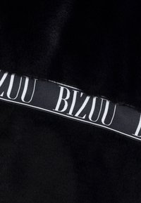 Zwart fauxbont stof met een satijnen lint waarop het woord "BIZUU" in het wit staat. Het lint contrasteert met de zachte textuur van het bont.