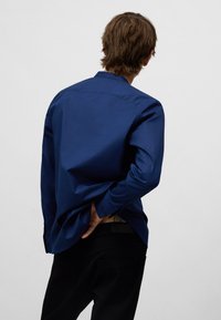 Marineblauw overhemd met lange mouwen, een klassieke kraag, een getailleerde pasvorm, knoopmanchetten en een gladde textuur, gedragen met zwarte broek.