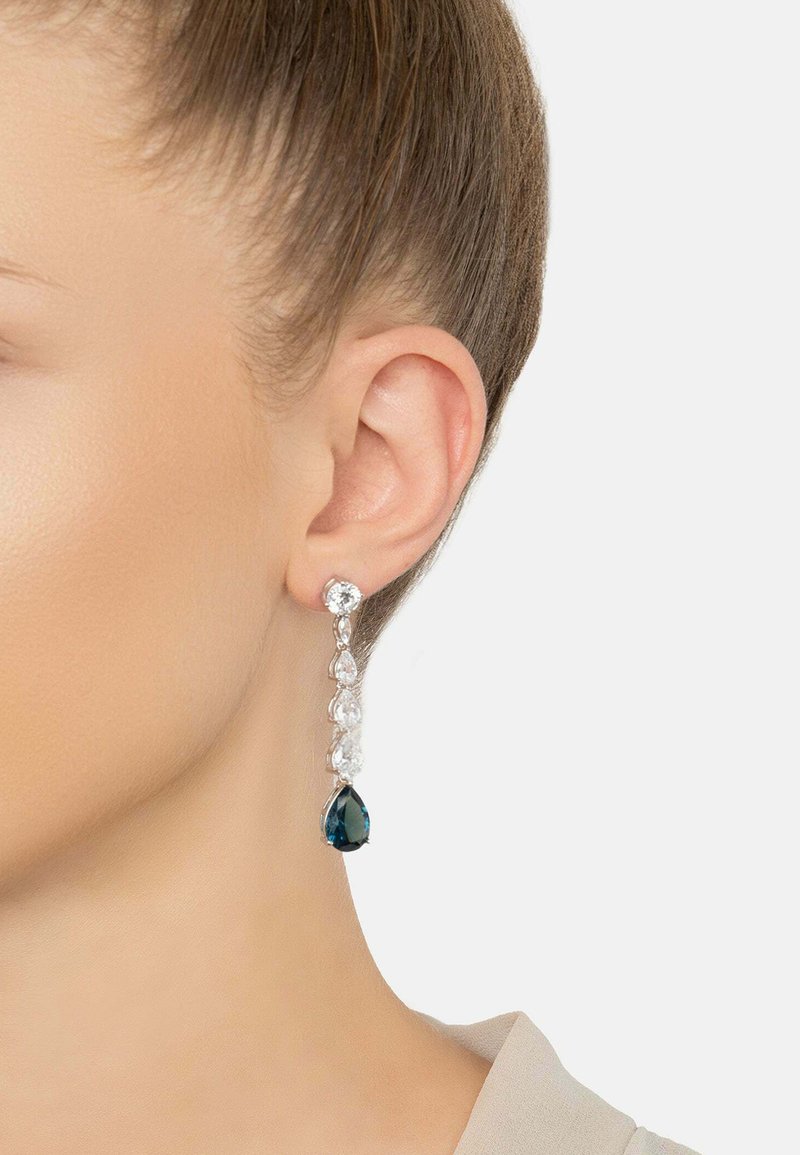 Silver drop earrings featuring clear and dark blue crystals, with a teardrop shape and a linear design, showcasing a reflective texture.