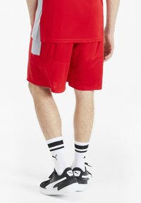 Rote Sportshorts mit kontrastierenden seitlichen Einsätzen, kombiniert mit schwarzen Turnschuhen und weißen Socken mit schwarzen Streifen.
