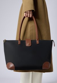 Borsa tote nera con dettagli in pelle marrone. Caratterizzata da una forma strutturata, manici arrotondati e una chiusura a flap con dettagli del logo.