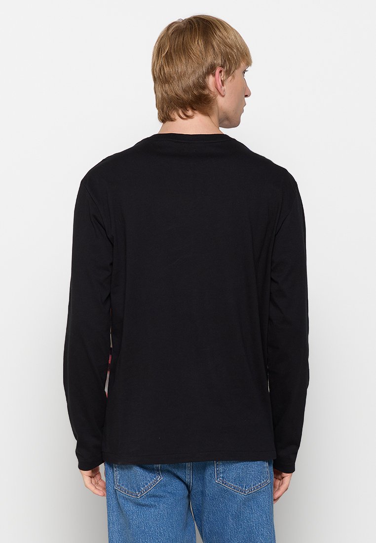 Schwarzes Langarm-T-Shirt aus Baumwolle mit Rundhalsausschnitt und geradem Schnitt, von hinten betrachtet. Kombiniert mit blauen Jeans.