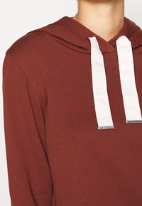 Maroon hoodie with a drawstring closure, featuring white flat laces with silver metal tips. Made from soft, textured fabric.